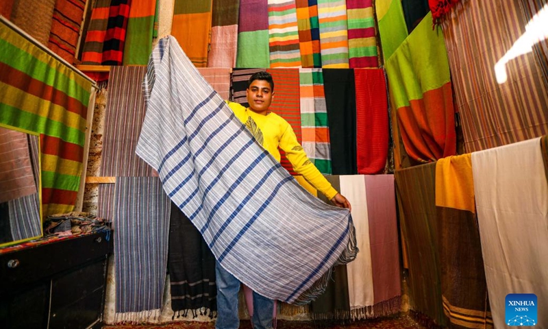 A man shows a woven scarf at Gharb Sohail village in Aswan, Egypt, on March 8, 2023. Gharb Sohail is a touristic Nubian village where visitors have a chance to know Nubians' unique traditions, crafts and food. Many people in the village now rely on the weaving industry to attract tourists.(Photo: Xinhua)