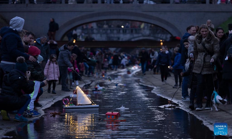 People look at miniature boats floating down a river in Ljubljana, Slovenia on March 11, 2023. According to the Slovenian old calendar, March 12 marks the start of Spring. It is a local tradition to send off miniature boats downstream on March 11 to celebrate Spring's arrival. (Photo:Xinhua)