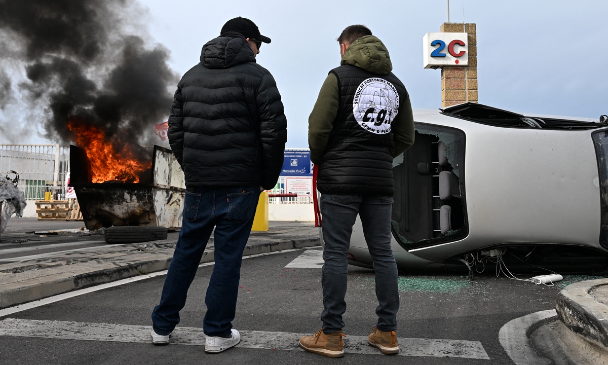 Dockers stand next to a fire and a destroyed car at an entrance to Marseille-Fos Port blocked during a rally called by French union General Confederation of Labour against the French government's proposed pensions reform, in Marseille on March 14, 2023. Photo: AFP