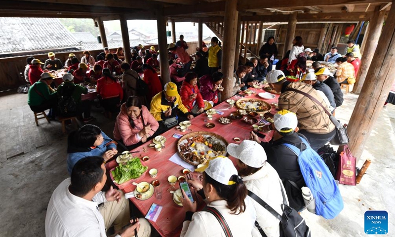 Tourists from Zhanjiang City of south China's Guangdong Province taste local food in Mengwu Miao Village, Rongshui Miao Autonomous County, south China's Guangxi Zhuang Autonomous Region, on March 19, 2023. More than 600 tourists from Zhanjiang took a special tourist train to Rongshui Miao Autonomous County to experience the charm of ethnic culture. (Xinhua/Huang Xiaobang)
