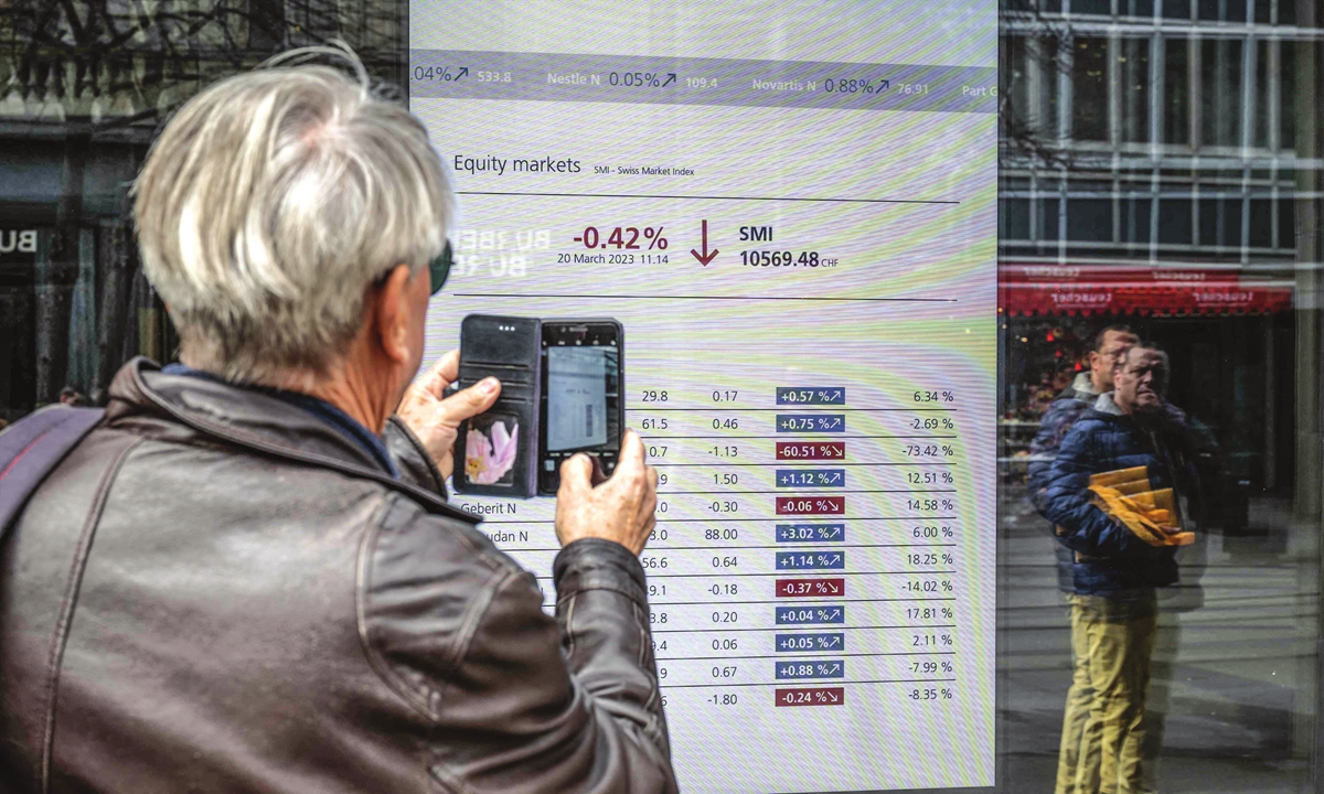A man takes a picture with his mobile phone of a market board at the headquarters of Swiss banking giant UBS in Zurich on March 20, 2023. UBS share prices plunged on March 20, 2023 as a deal to take over its troubled Swiss rival Credit Suisse for $3.25 billion failed to calm stock market nerves. Photo: VCG