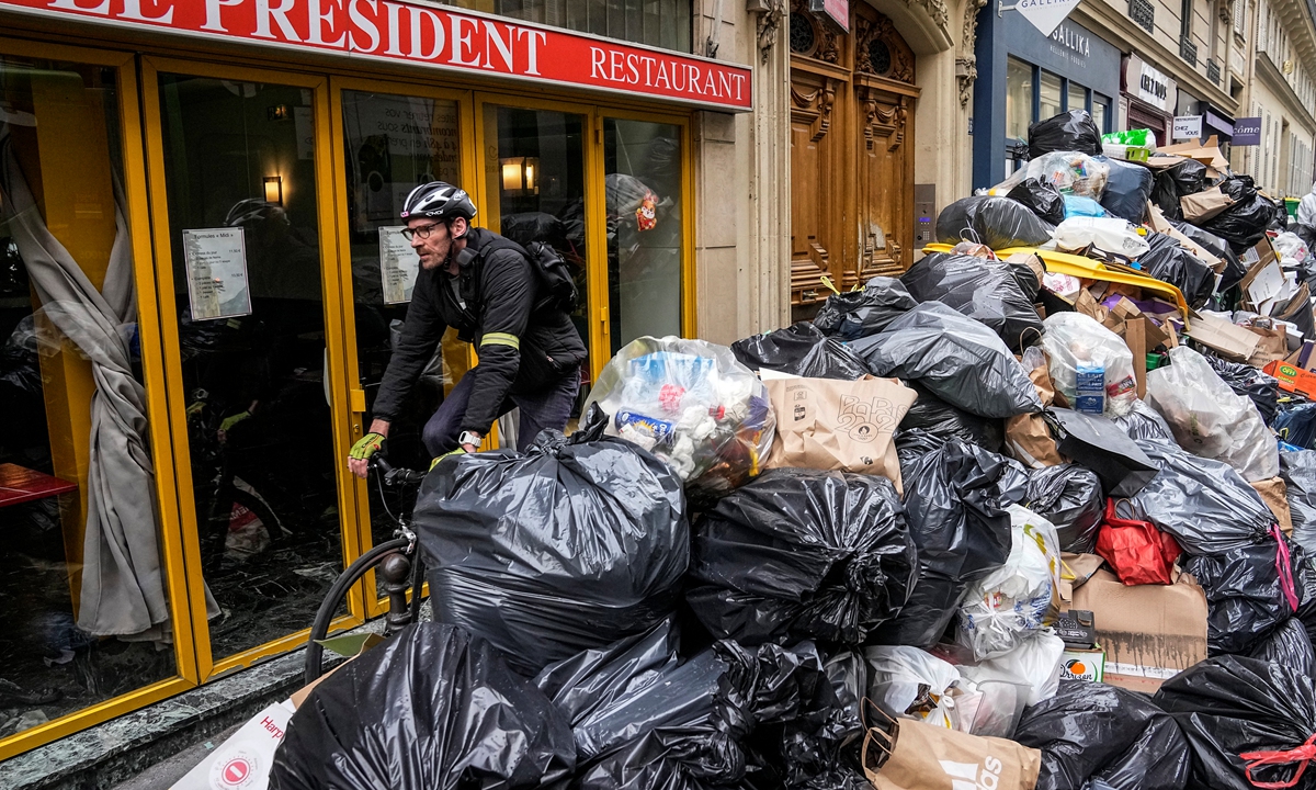 A cyclist rides past an uncollected garbage pile in Paris on March 21, 2023, as the large-scale strike continues due to a pension reform bill pushed through by French President Emmanuel Macron without lawmakers' approval. The bill still faces a review by the Constitutional Council before it can be signed into law. Photo: CFP