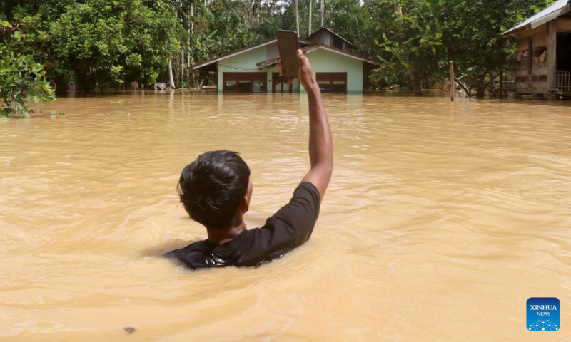 A man holds his cell phone to contact his relative in flood water after heavy rain in Napai village in Aceh Barat district, Aceh Province, Indonesia, May 7, 2023. (Photo by Yulham/Xinhua)