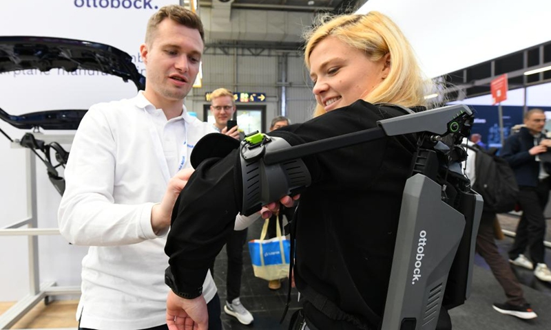 A visitor (R) tries an exoskeleton equipment at Hannover Messe 2023 in Hannover, Germany, April 20, 2023. The trade fair, one of the world's largest and lasting from April 17 to April 21, showcases more than 4,000 companies, which present solutions for the production and energy supply of the future.(Photo: Xinhua)