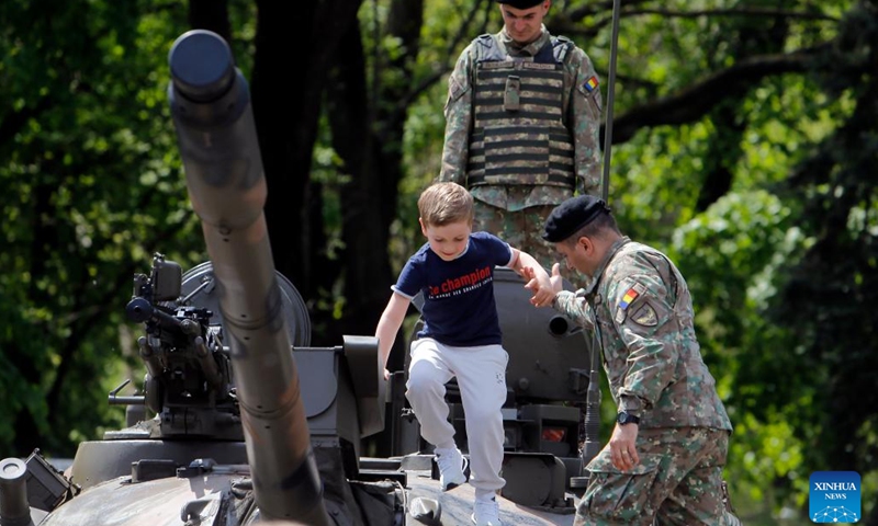 A Romanian soldier helps as a child steps on a tank at a static exhibition of military equipment marking Romanian Land Forces Day at a park in Bucharest, capital of Romania, April 23, 2023.(Photo: Xinhua)