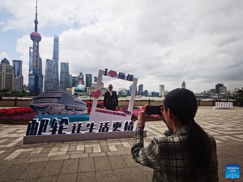 A man poses for photo by a decoration themed on Adora Magic City along the Huangpu River in Shanghai, east China, May 19, 2023. (Xinhua/Chen Aiping)