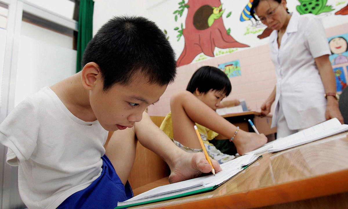 Two Vietnamese students, both Agent Orange victims and living with disabilities, learn to write with their feet at a hospital in Ho Chi Minh City on March 3, 2005. Photo: VCG