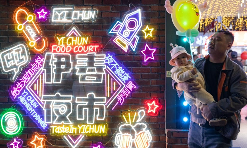 A man holds a child at a night market in Yichun, northeast China's Heilongjiang Province, May 19, 2023. The night market in Yichun has attracted a lot of tourists, which boosts its nighttime economy. (Xinhua/Zhang Tao)