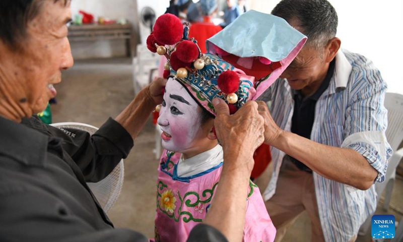 Elderly folk artists help 9-year-old Anhui Opera student Fang Dongdong (C) wear a headdress at Fuling Village of Jixi County, Xuancheng City, east China's Anhui Province, May 30, 2023. In order to promote Anhui Opera and raise awareness of the traditional performing art, a primary school in Fuling Village has been offering a routine training program since 2003 for its students, hiring veteran folk artists as tutors.(Photo: Xinhua)