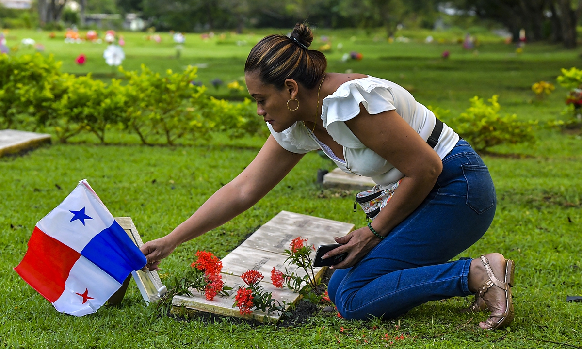 A woman puts a Panamanian national flag over the grave of relative killed in the 1989 US military invasion to Panama, during a ceremony commemorating the 30th anniversary of the invasion, at the Jardin de la Paz cemetery in Panama City, on December 20, 2019. Photo: AFP