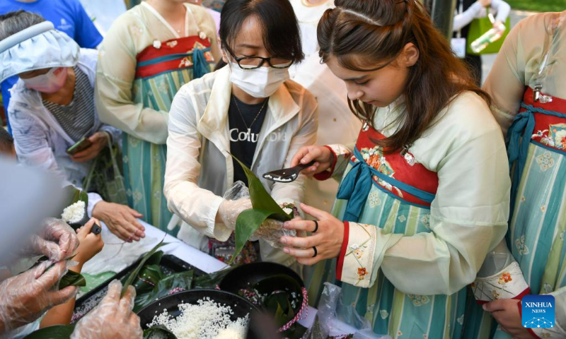 A French girl (R front) learns to make Zongzi,a pyramid-shaped dumpling made of glutinous rice wrapped in bamboo or reed leaves, at Longtan Park in Beijing, capital of China, June 22, 2023. A series of activities including boat races, performances, interactive games were held during the Dragon Boat Festival here. (Xinhua/Ju Huanzong)