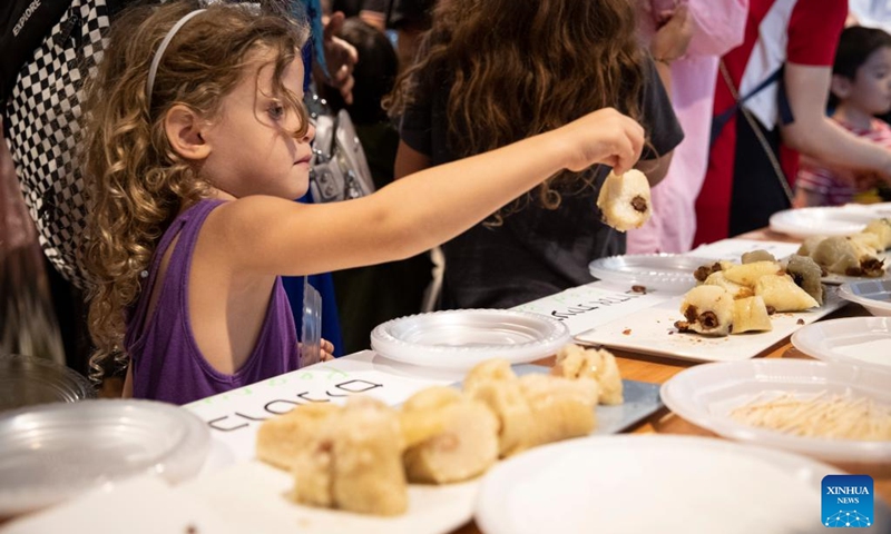 A girl tries to eat Zongzi, a traditional Chinese food, during a celebration of Dragon Boat Festival at the China Cultural Center in Tel Aviv, Israel, on June 22, 2023. (Xinhua/Chen Junqing)