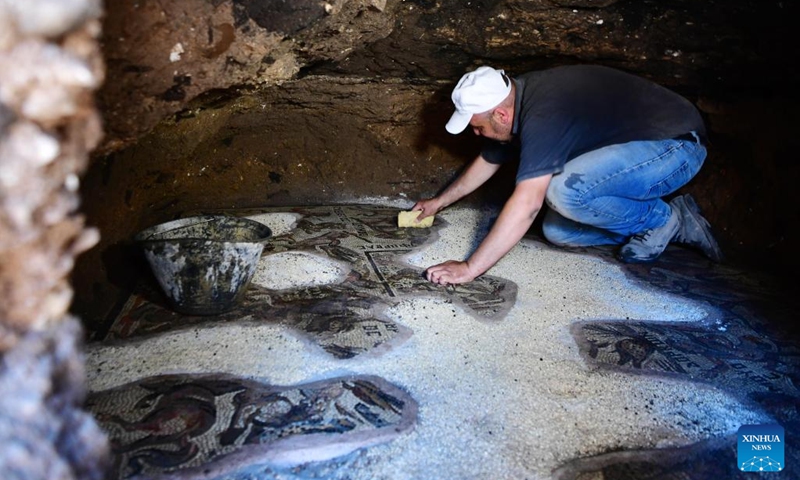 An archeologist cleans a Roman-era mosaic panel recently uncovered in the city of al-Rastan in Homs, Syria, on June 22, 2023. (Photo by Ammar Safarjalani/Xinhua)