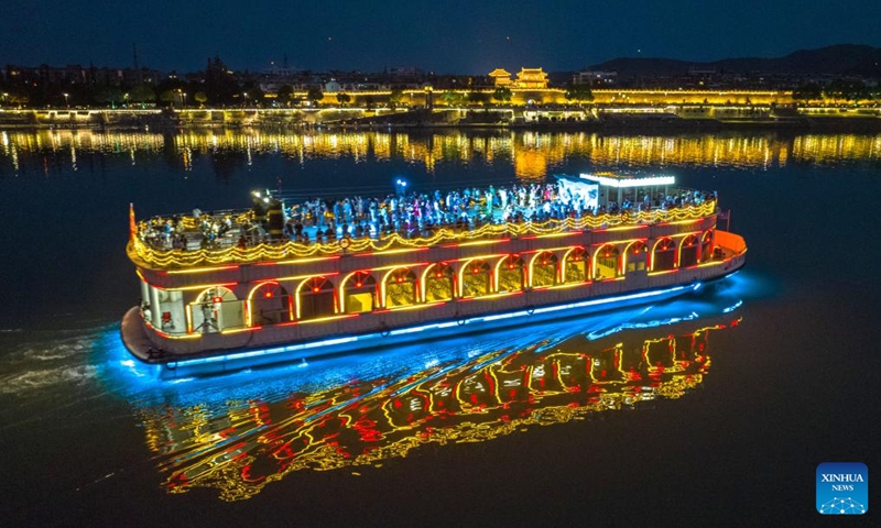 This aerial photo shows tourists aboard a ship for night sightseeing of an ancient town in Xiangyang City, central China's Hubei Province, June 22, 2023. People go out for various activities during the three-day Dragon Boat Festival holiday across the country. (Photo by Yang Dong/Xinhua)