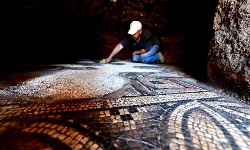 An archeologist cleans a Roman-era mosaic panel recently uncovered in the city of al-Rastan in Homs, Syria, on June 22, 2023. (Photo by Ammar Safarjalani/Xinhua)