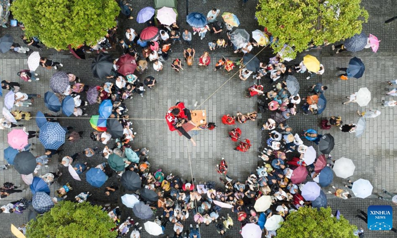 This aerial photo shows tourists watching Nuo Opera performance at the Hong'an ancient town in Xiushan Tujia and Miao Autonomous County, southwest China's Chongqing, June 22, 2023. People go out for various activities during the three-day Dragon Boat Festival holiday across the country. (Photo by Hu Cheng/Xinhua)
