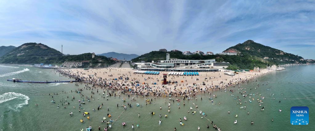 This aerial panoramic photo shows tourists playing at a beach in Lianyungang, east China's Jiangsu Province, June 23, 2023. People go out for various activities during the three-day Dragon Boat Festival holiday across the country. (Photo by Wang Chun/Xinhua)