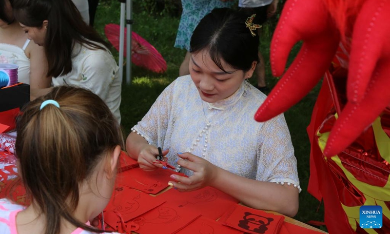 A staff member makes paper cutting works at a dragon boat cultural festival in Sofia, Bulgaria, June 24, 2023. Bulgaria's first dragon boat cultural festival kicked off at Pancharevo Lake in the capital city of Sofia on Saturday. (Xinhua/Lin Hao)