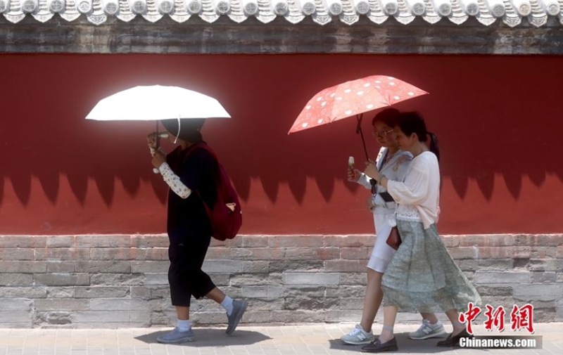 Pedestrians holding umbrellas to shield from the sun and heat walk in the street in Beijing, June 23, 2023. (Photo: China News Service/Jia Tianyong)


