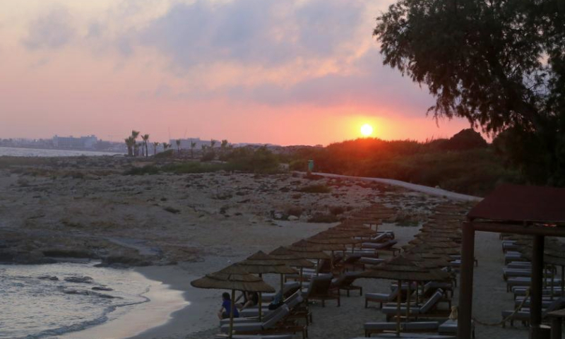 This photo taken on June 26, 2023 shows the sunset near the Bridge of Lovers at the seaside of Ayia Napa, Cyprus. The Bridge of Lovers, a natural rocky arch bridge at the seaside of Ayia Napa, has attracted many visitors. (Xinhua/Guo Mingfang)