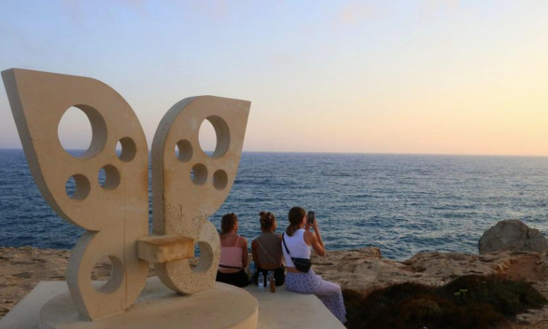 This photo taken on June 26, 2023 shows the sunset near the Bridge of Lovers at the seaside of Ayia Napa, Cyprus. The Bridge of Lovers, a natural rocky arch bridge at the seaside of Ayia Napa, has attracted many visitors. (Xinhua/Guo Mingfang)