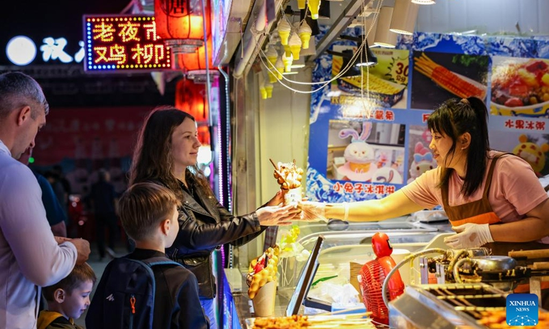 Russian tourists buy snacks during their visit to a night market in Hunchun, northeast China's Jilin Province, June 27, 2023. Hunchun, a city with about 220,000 residents, is located at China's border with Russia and the Democratic People's Republic of Korea. The resumption of passenger services by the Hunchun customs at the start of 2023 has made it convenient for Russian tourists who visit the city for shopping, entertainment and food experiences.(Photo:Xinhua)