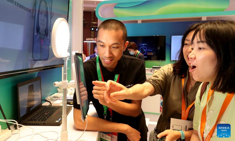 A staff member helps visitors try a health check-up device via face scanning at the 2023 Amazon Cloud Technology China Summit in Shanghai, east China, June 28, 2023. The 2-day summit concluded here on Wednesday, showcasing advanced technologies including VR, AI and cloud computing. (Photo: Xinhua)