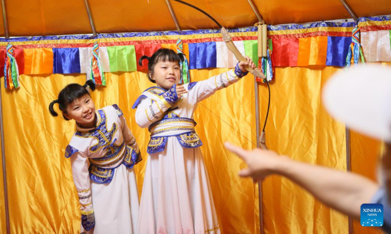 Children try on ethnic costumes and pose for photos at a night fair at Minhang Museum of Shanghai in east China to experience the traditional Mongolian custom, July 21, 2023. (Xinhua/Xin Mengchen)