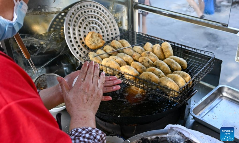 A woman makes fried cakes at her stall in the Northwest Corner of Tianjin, north China, July 10, 2023. The Northwest Corner is named due to its location in the northwest corner of the old city of Tianjin. In the morning, many tourists who speak various dialects drag their suitcases here to have breakfasts with Tianjin characteristics.(Photo: Xinhua)