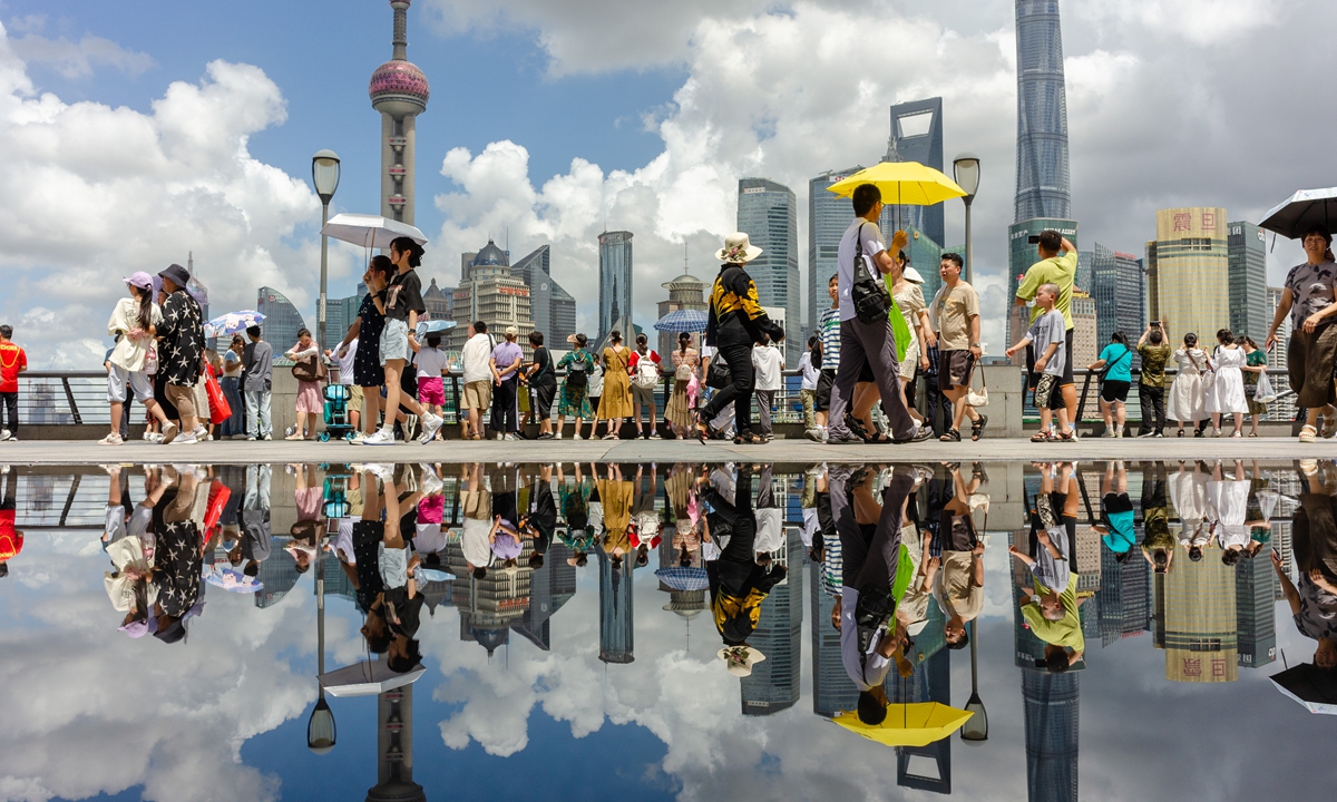 Tourists and the buildings in Lujiazui, the financial district in Shanghai, are reflected in a puddle left on the street in Shanghai on July 17, 2023 after scattered showers, presenting the beauty of a “land of the sky.” Photo: VCG