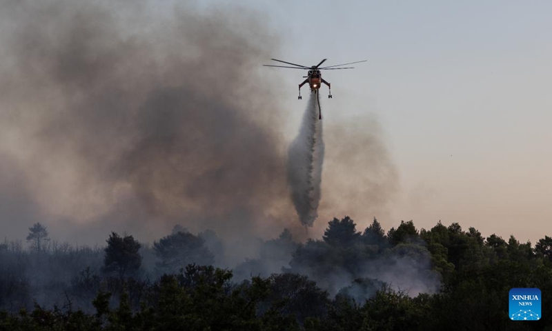 This photo taken on July 18, 2023 shows a helicopter trying to extinguish a wildfire in Mandra, a western suburb of Athens, Greece. Hundreds of Greek firefighters continued for a second day on Tuesday to battle two major wildfires near Dervenochoria, some 30 km northwest of Athens, and near the seaside resort of Loutraki, about 80 km southwest of the capital, authorities said.(Photo: Xinhua)