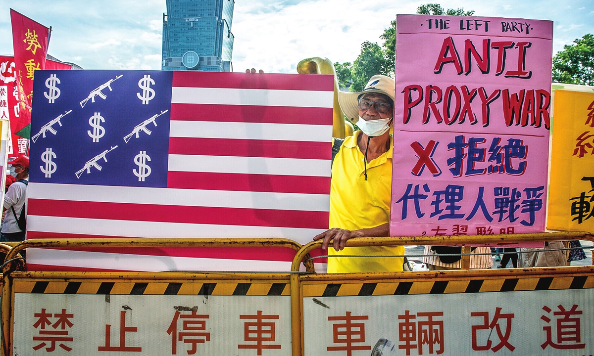 Residents protest in Taipei with an American flag showing guns and dollars and a banner saying 