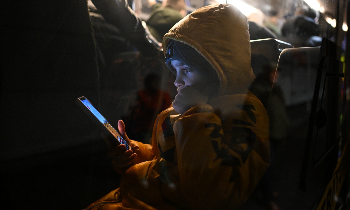 A Ukrainian boy who fled the war and found shelter in a former supermarket converted for a refugee center plays on his smartphone inside a bus to take him and others to an evacuation train to Hannover on February 17, 2023, in Przemysl, Poland. Photo: VCG