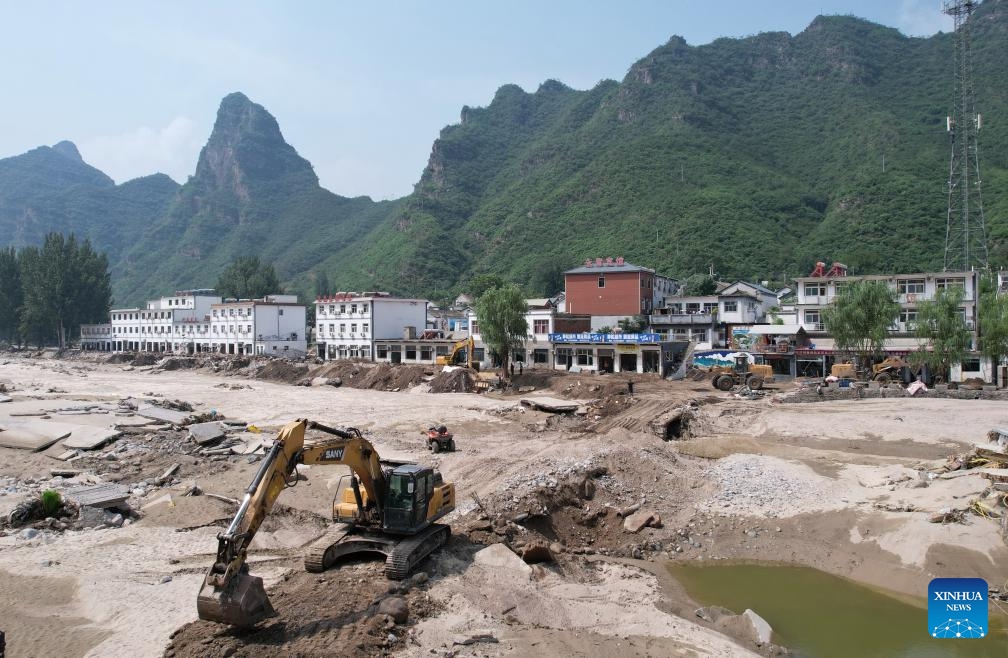 This aerial photo taken on Aug. 9, 2023 shows workers operating machinery to repair a road leading to Shangzhuang Village of Sanpo Town, Laishui County, north China's Hebei Province. Some roads blocked by the rain-triggered floods in the county are repaired, and electricity and communication services are restored.(Photo: Xinhua)