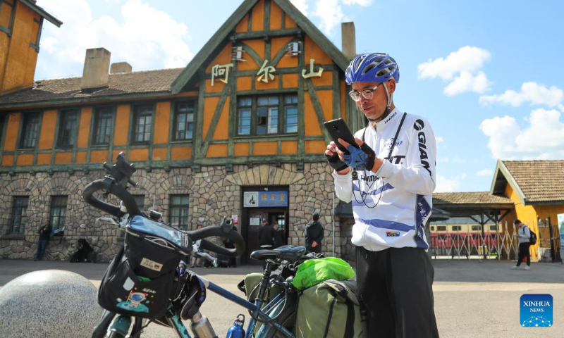 A cyclist takes pictures in front of the train station of Arxan in Hinggan League, north China's Inner Mongolia Autonomous Region, Sept. 1, 2023. Arxan, located at the southwestern foot of the Dahinggan Mountains and at the intersection of four major grasslands, is an increasingly popular tourist destination. (Xinhua/Wang Kaiyan)