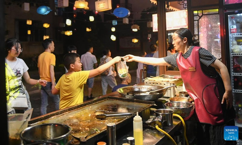 A child buys snacks at a night fair in Xuan'en County of Enshi Tujia and Miao Autonomous Prefecture, central China's Hubei Province, Aug. 18, 2023. A series of activities have been held to boost the nighttime economy in the scenic area of Xuan'en County including sightseeing trips on the Gongshui River and night fairs along the river. (Xinhua/Cheng Min)