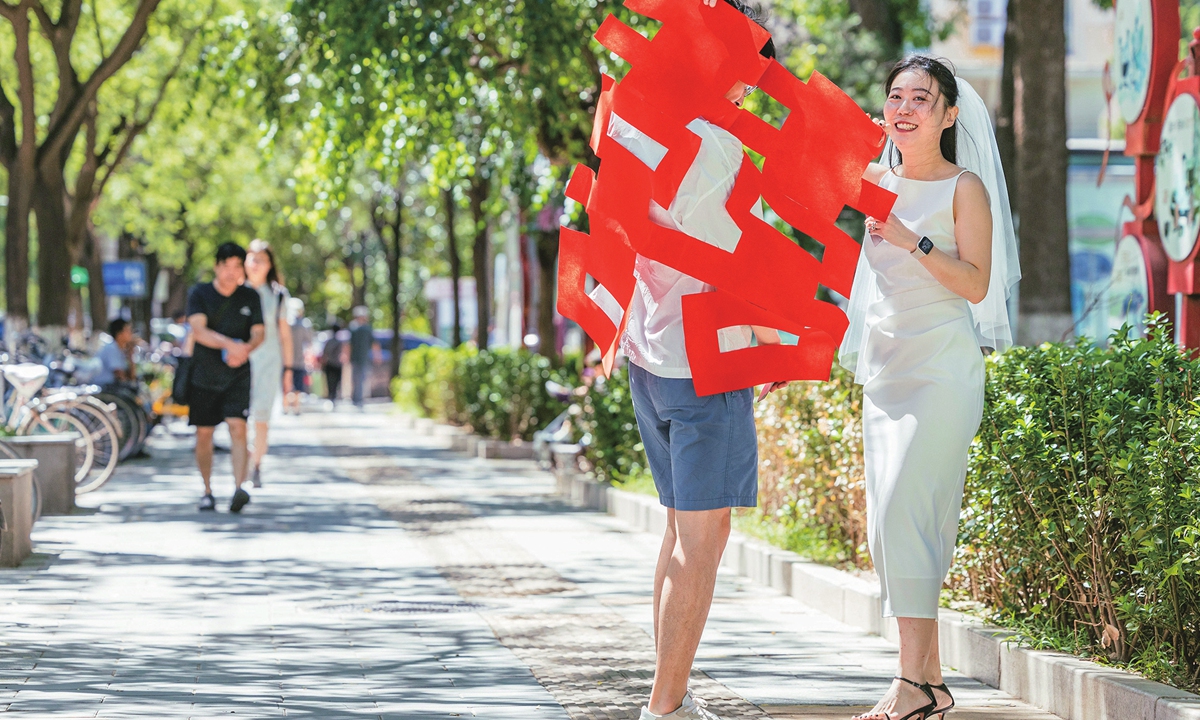 Newlyweds hold a giant paper cutting shaped as the Chinese character xi or 