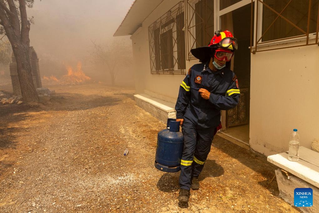 A firefighter removes a gas tank from a building near Athens, Greece, on Aug. 23, 2023. Wildfires raging around Greece's capital spread to the Mount Parnitha National Park, northwest of Athens, on Wednesday, the Fire Brigade said. The blaze that broke out on Tuesday at the mountain's foot has already damaged homes and scorched forested land. Nearby settlements and a migrant camp were evacuated as a precautionary measure.(Photo: Xinhua)