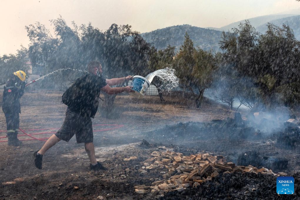 A firefighter and a volunteer try to extinguish a wildfire near Athens, Greece, on Aug. 23, 2023. Wildfires raging around Greece's capital spread to the Mount Parnitha National Park, northwest of Athens, on Wednesday, the Fire Brigade said. The blaze that broke out on Tuesday at the mountain's foot has already damaged homes and scorched forested land. Nearby settlements and a migrant camp were evacuated as a precautionary measure.(Photo: Xinhua)