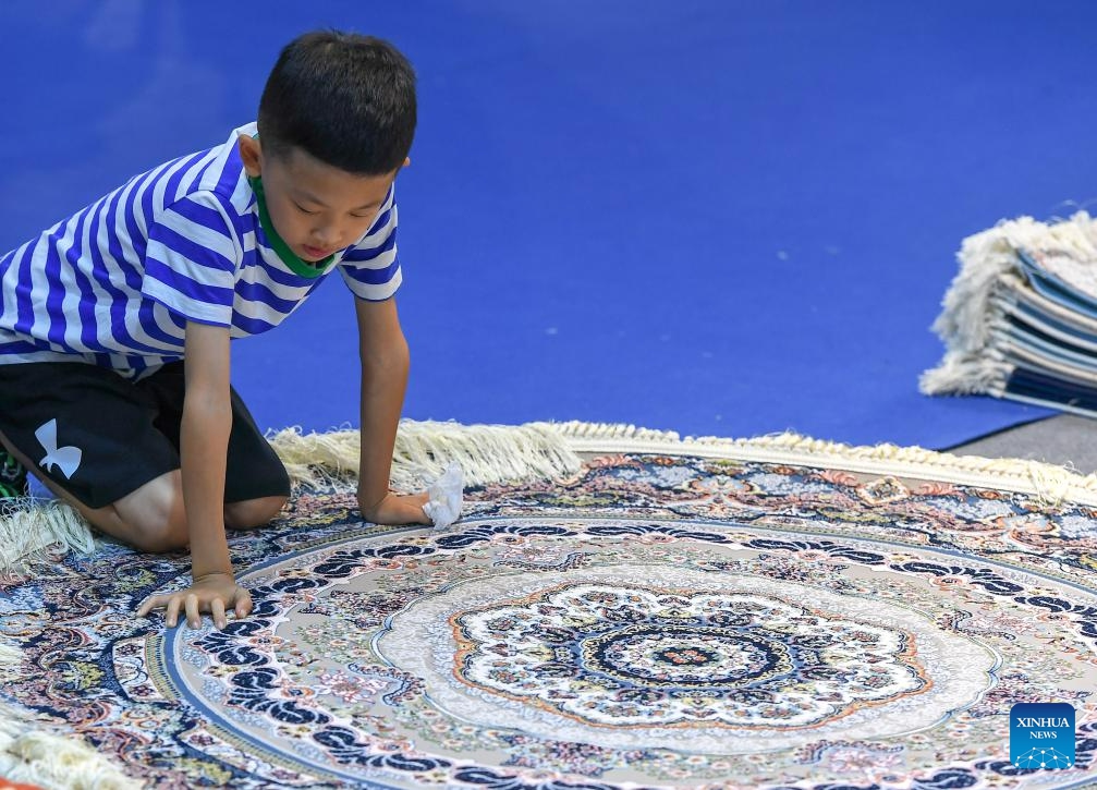 A child touches a carpet from Iran at the 14th China-Northeast Asia Expo in Changchun, the capital city of northeast China's Jilin Province, Aug. 23, 2023. The 14th China-Northeast Asia Expo opened Wednesday in Changchun. The five-day event, scheduled both online and offline, has attracted more than 1,000 companies from home and abroad, with a predominant representation from countries in Northeast Asia.(Photo: Xinhua)
