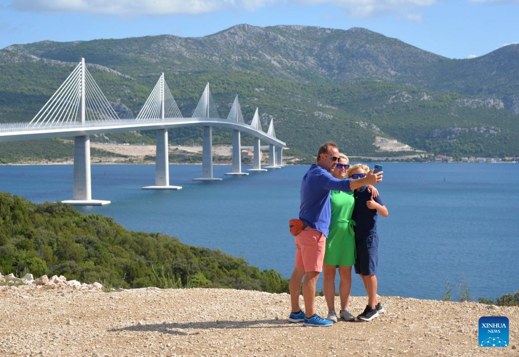 People take souvenir photos in front of the Peljesac Bridge in Komarna, Croatia, on Aug. 29, 2023. The Peljesac Bridge in the south of Croatia, built by a Chinese consortium led by the China Road and Bridge Corporation (CRBC), connects the Croatian mainland with the Peljesac peninsula, giving the country a continuous land link that bypasses Bosnian territory.(Photo: Xinhua)