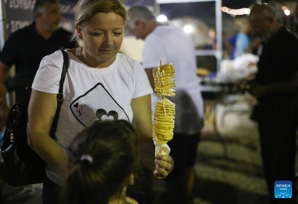 A woman holds a potato skewer during an international potato festival in the village of Xylofagou, Cyprus, on Sept. 7, 2023. An international potato festival kicked off on Thursday in the village of Xylofagou, which is renowned for its potato production.(Photo: Xinhua)