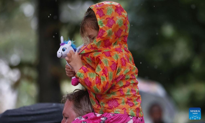 A girl tries to cover her toy in her raincoat in the rain in Paris, France, Sept. 12, 2023.(Photo: Xinhua)