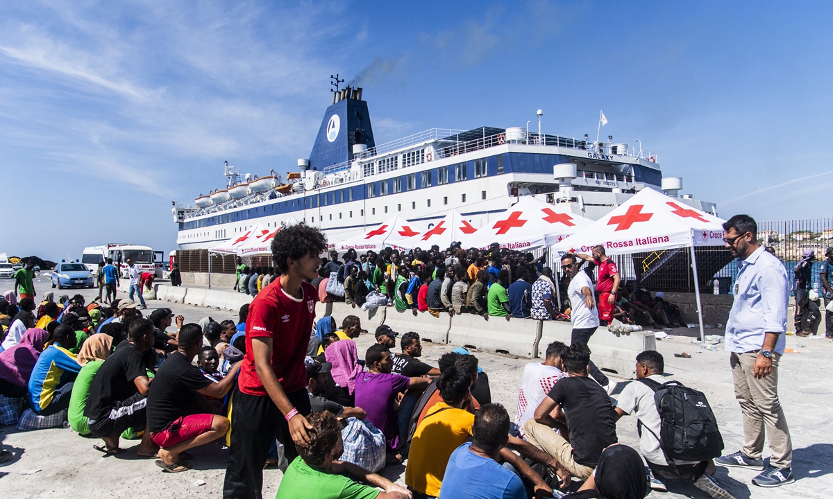 Migrants from a migrant housing center on the Italian island of Lampedusa are guided by a security official on September
14, 2023, as they prepare to board the ship <em>Galaxy</em>, bound for the Sicilian town of Porto Empedocle. The tiny Italian island
struggled to cope with a recent surge in migrant boats from North Africa. Photo: AFP