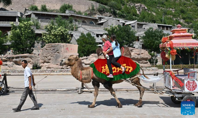 Villager Liu Jintu (L) leads his camel in the Qikou ancient town of Linxian County, north China's Shanxi Province, Aug. 2, 2023. Seeing the rapid development of tourism in the Qikou ancient town, Liu quit his job at construction sites. He bought a camel in 2016 and provided it to tourists for rides. Qikou, an ancient riverine town along the Yellow River, was an important trade ferry in history. However, with the development of land transportation, the Qikou ancient town declined in terms of trade volume, leaving many of its historical buildings in disrepair. In recent years, local authorities have carried out protection and restoration of historical buildings and ancient dwellings in the Qikou ancient town. At the same time, the integrated development of culture and tourism is also promoted. Today the ancient town has become a popular tourist attraction. More than 5,000 people out of a population of about 30,000 in the town are engaged in the tourism industry.(Photo:Xinhua)