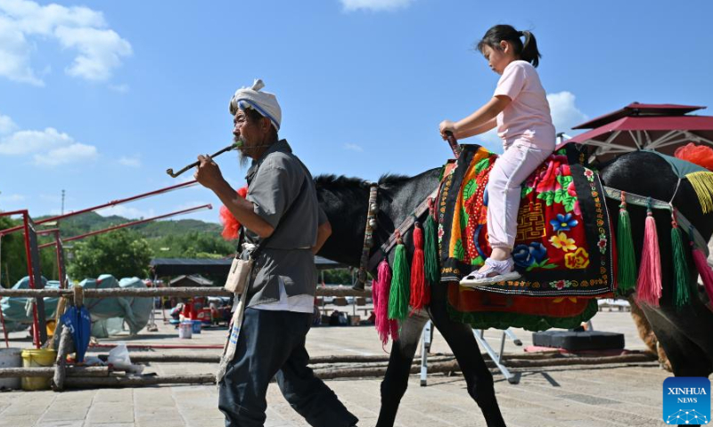Villager Li Yonglin leads his donkey in the Qikou ancient town of Linxian County, north China's Shanxi Province, Aug. 2, 2023. Li would decorate his donkey and provide it to tourists for riding amid slack season of agricultural production. Qikou, an ancient riverine town along the Yellow River, was an important trade ferry in history. However, with the development of land transportation, the Qikou ancient town declined in terms of trade volume, leaving many of its historical buildings in disrepair. In recent years, local authorities have carried out protection and restoration of historical buildings and ancient dwellings in the Qikou ancient town. At the same time, the integrated development of culture and tourism is also promoted. Today the ancient town has become a popular tourist attraction. More than 5,000 people out of a population of about 30,000 in the town are engaged in the tourism industry. (Photo:Xinhua)