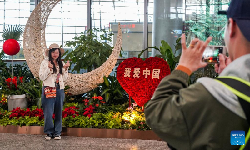 A passenger poses for photos in front of flower decorations at Kunming Changshui International Airport in Kunming, southwest China's Yunnan Province, Sept. 27, 2023. The Mid-Autumn Festival and National Day holiday period, which will last from Sept. 29 to Oct. 6 this year, is a peak travel and tourism season in China. (Xinhua/Cui Wen)