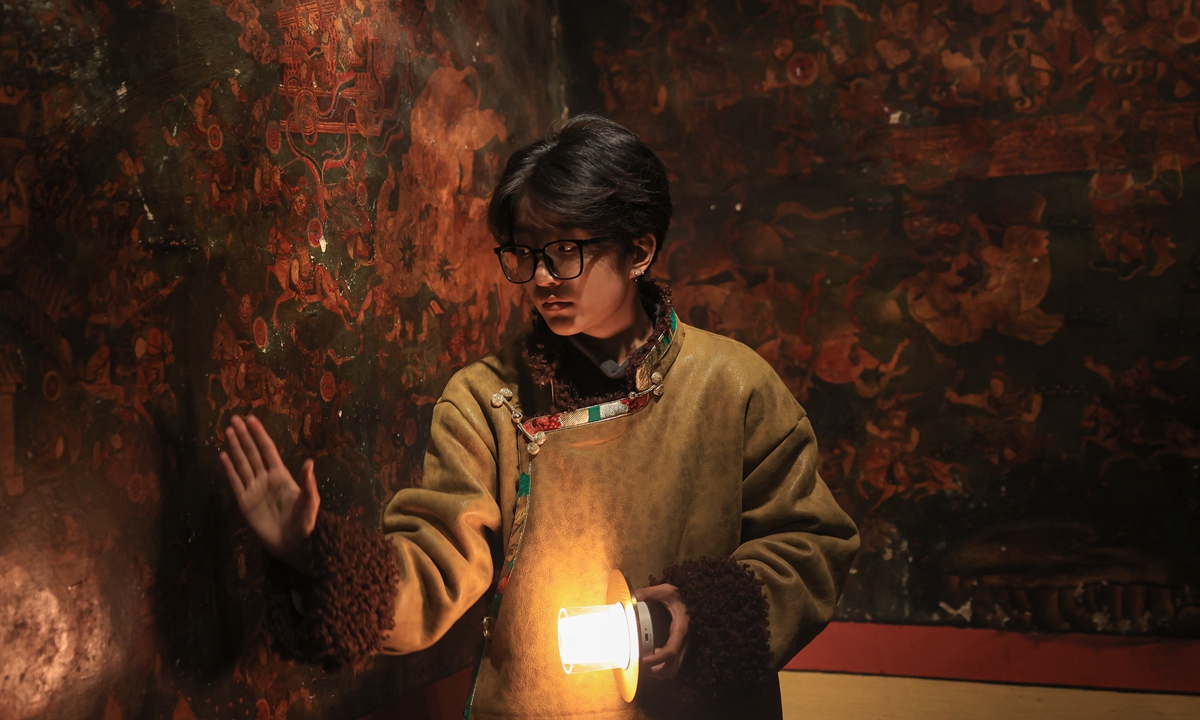 A tour guide at the Jebum-Gang Art Center shows details of the wall paintings at the center to thee visitors with light. Photo: Shan Jie/GT