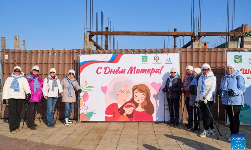Participants of the Nordic walking race pose for pictures in front of a giant poster in Vladivostok, Russia, Nov. 26, 2023. A Nordic walking race was held in the Russian Far East city of Vladivostok to commemorate the Mother's Day of the country, which falls on the last Sunday of November. (Photo: Xinhua)