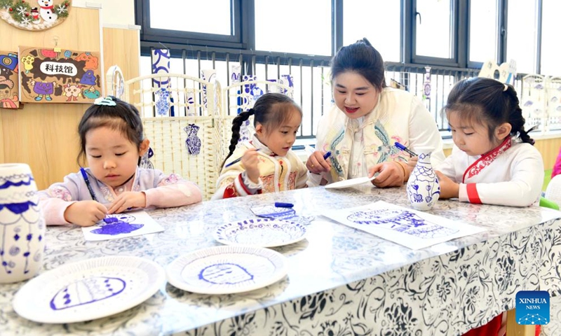 Teacher Li Tianyi teaches children to draw patterns of blue-and-white porcelain on paper plates at Shanwang kindergarten in Jinan, east China's Shandong Province, Nov. 29, 2023. Shanwang kindergarten has set up many workshops for children to learn about traditional Chinese culture. Kids could receive various art education like shadow play, traditional Chinese painting and tie-dye techniques from teachers according to their interests.(Photo: Xinhua)